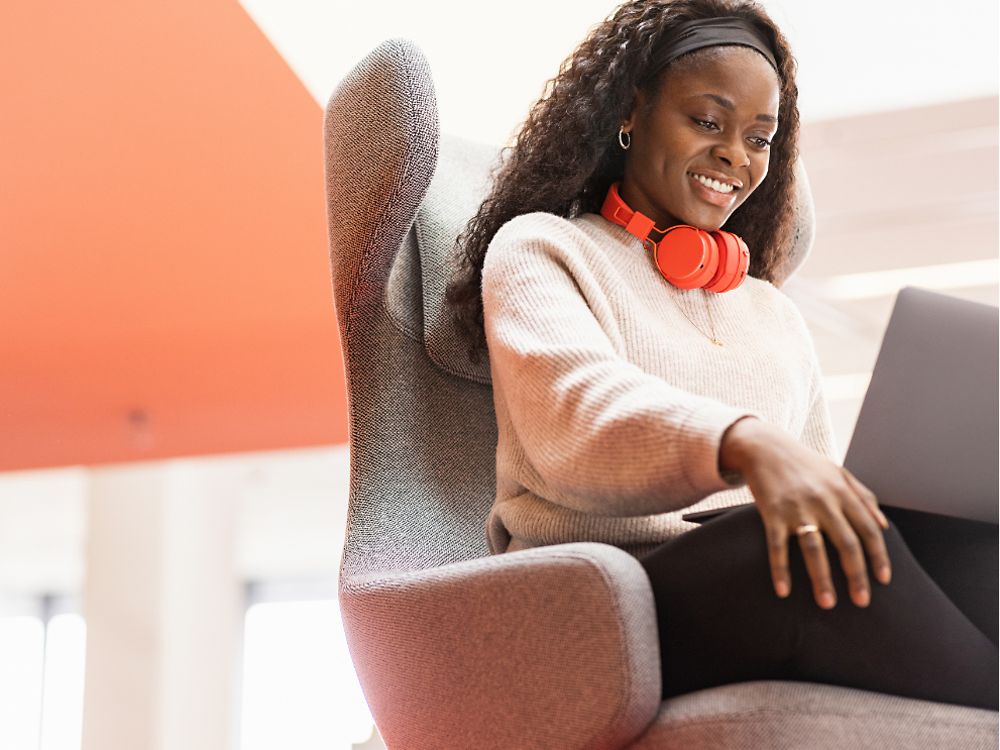 En Henkel-ansatt sitter i en komfortabel stol med den bærbare datamaskinen på knærne. Hun smiler. 