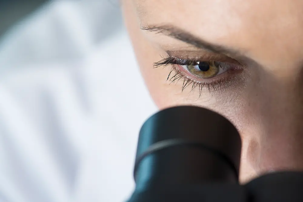 Øye av en kvinne som ser inn i et mikroskop