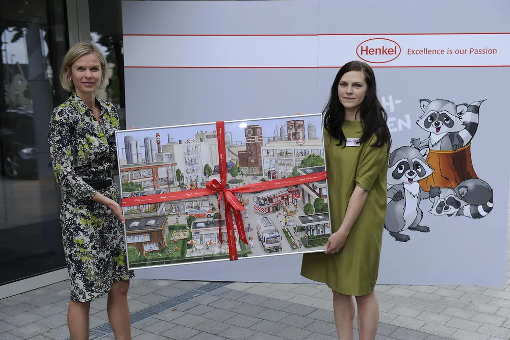 Kathrin Menges übergibt das Begrüßungsgeschenk an Ina Eisenmann, Leiterin der neuen Henkel-KiTa „Die Waschbären“.